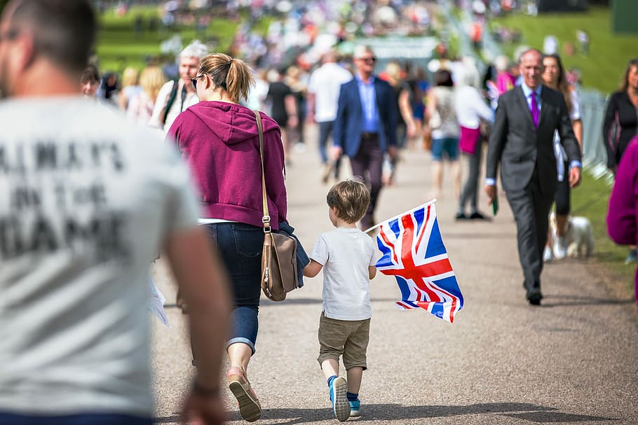selective focus photography of boy holding U.K. flag walking on pathway full of people, boy holding United Kingdom flag in front of crowded people, HD wallpaper