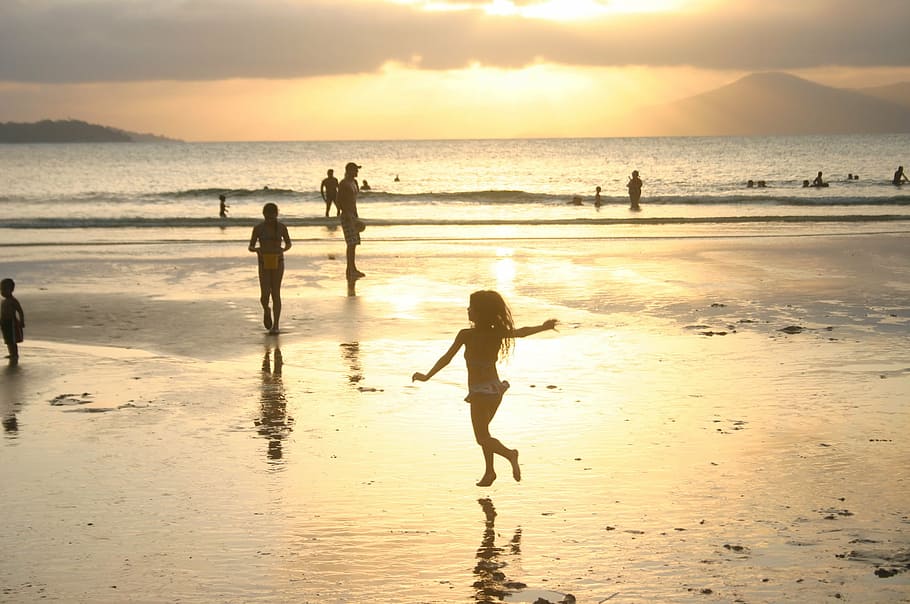 silhouette of girl playing on seashore near people on beach during sunset HD wallpaper