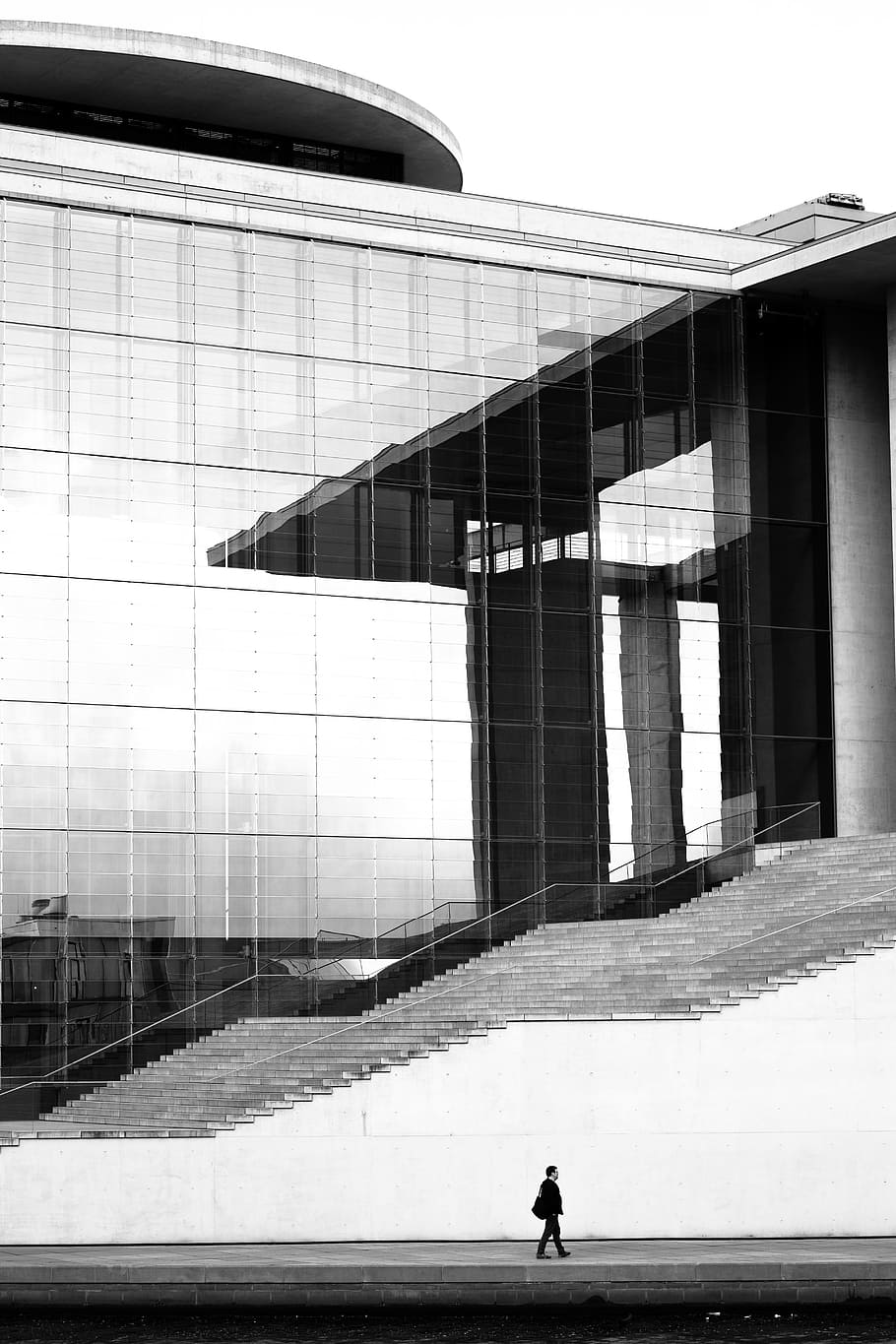 grayscale photo of man walking on concrete pavement beside high building, person walking on building during daytime HD wallpaper