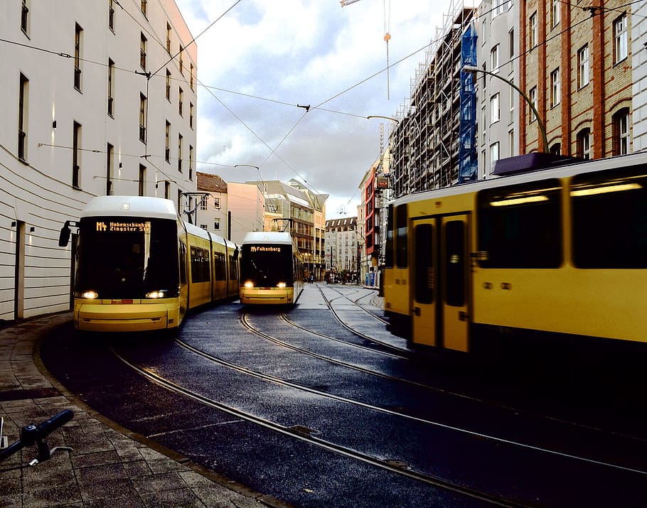 three yellow cable trains moving on road in between buildings at daytime HD wallpaper