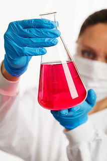 person in white laboratory gown and blue gloves holding clear glass laboratory flask with red liquid HD wallpaper