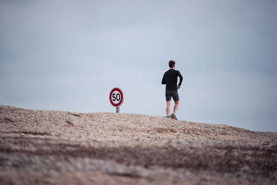 man wearing black top standing near road signage during daytime, man running in the mountain HD wallpaper