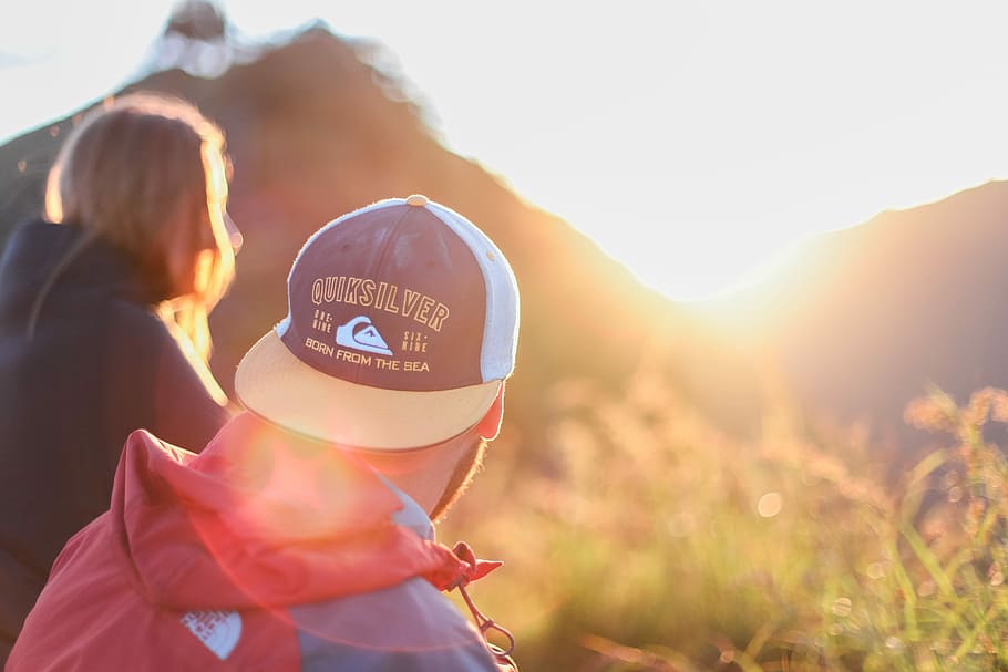 shallow photography of of man and woman sitting looking at sun rise, man wearing white and blue flat brimmed cap and red The North Face windbreaker, HD wallpaper