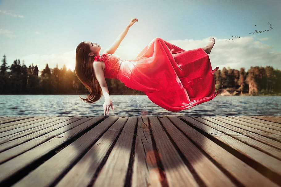 woman in red sleeveless dress floating above brown wooden dock during daytime HD wallpaper