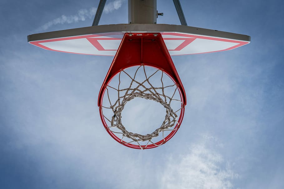 high-angle photography of red and white basketball system, low-angle photography of red basketball hoop under cloudy sky