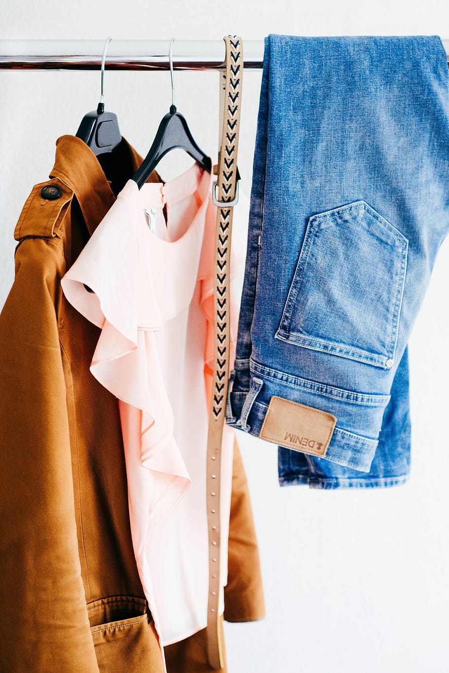 women's four assorted apparel hanged on clothes rack, blue jeans and brown coat hanging on black bar