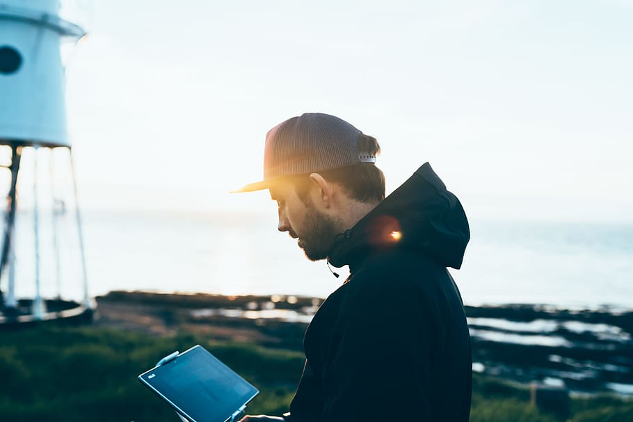 close-up photo of man with hat using tablet computer near sea, man holding tablet computer HD wallpaper
