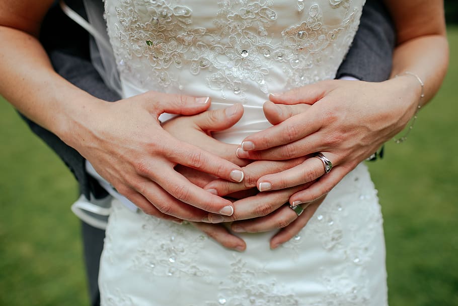 shallow focus photography of person hugging a person in white dress, man behind of woman while holding hands
