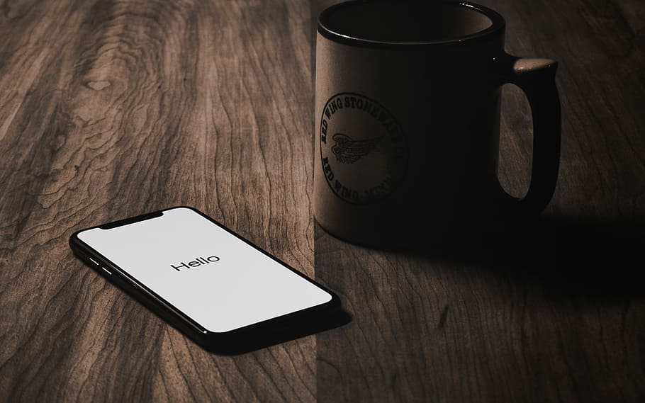 iPhone X on tabletop beside mug, turned on iPhone X beside brown ceramic mug on brown surface HD wallpaper