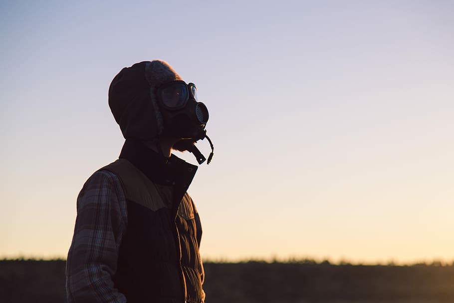 man standing on open field wearing respirator, person wearing black gas mask during daytime