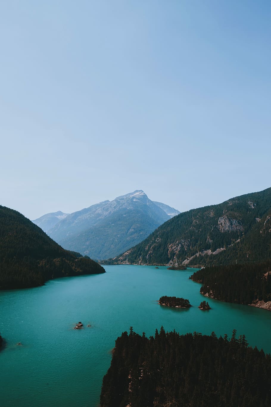 body of water between green and brown mountain range under clear blue sky during daytime, aerial photo of body of water surrounded by mountain HD wallpaper