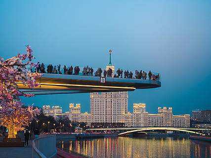 people standing beside gray concrete building near suspension bridge at night time, people standing on platform above the river HD wallpaper