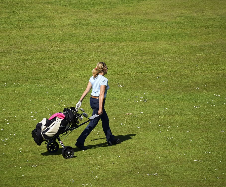 woman walking while holding golf trolley with golf set on grass field at daytime, HD wallpaper