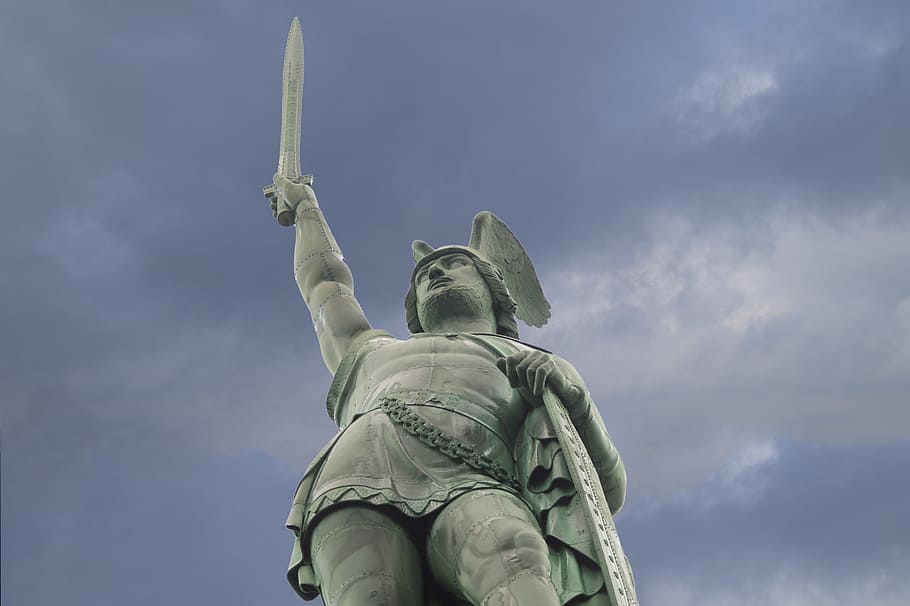 man raising sword and holding shield concrete statue under gray sky during daytime