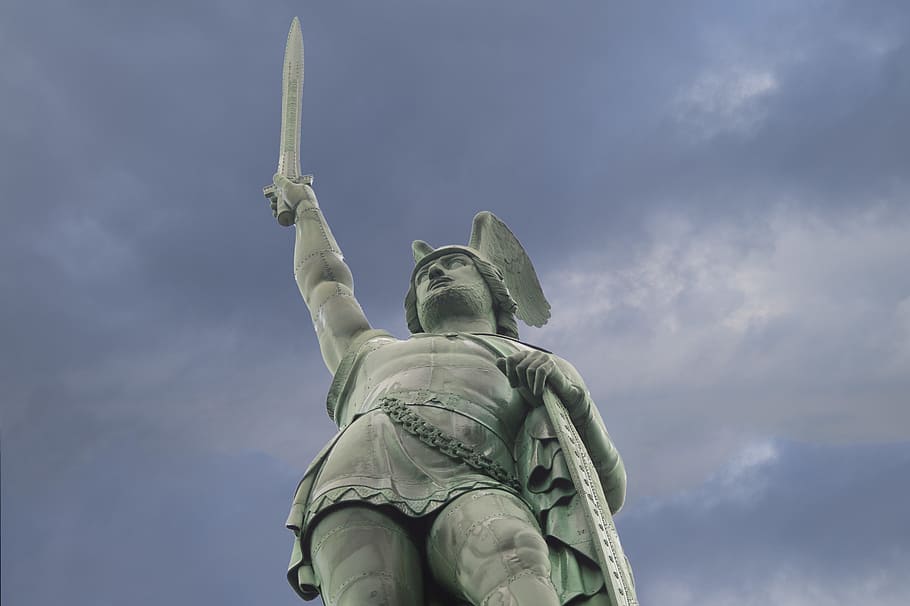 man raising sword and holding shield concrete statue under gray sky during daytime HD wallpaper