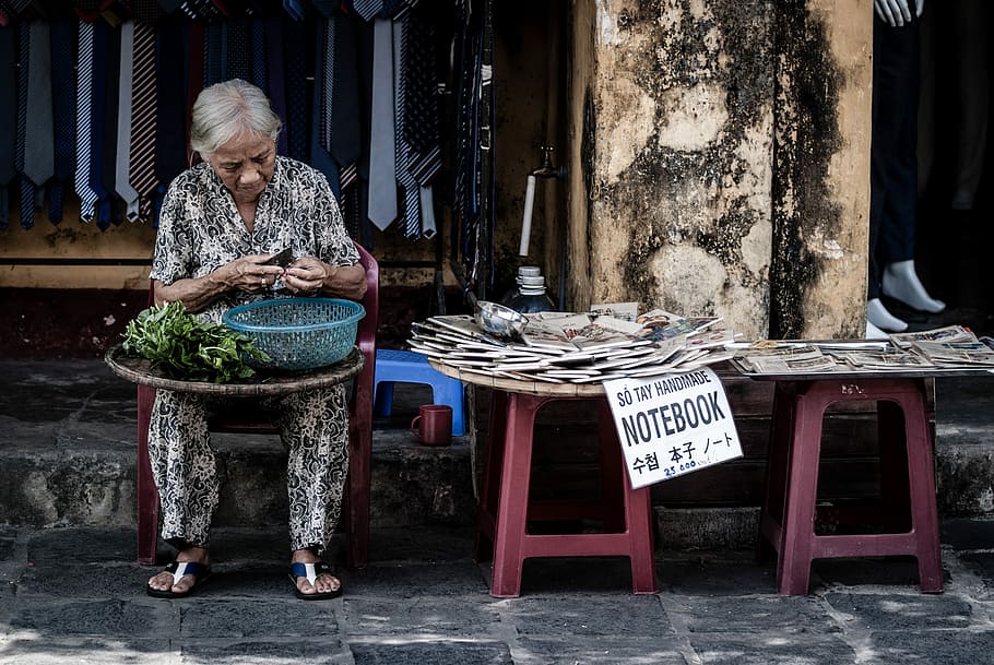 woman sitting on chair slicing vegetables, woman selling notebook in sidewalk
