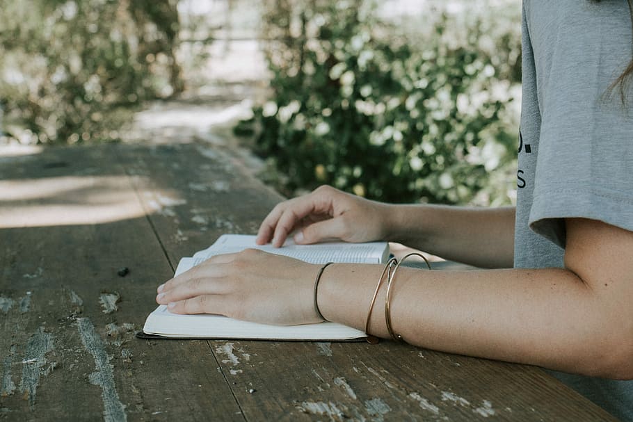 person holding book white sitting in front of desk, person reading book during daytime HD wallpaper
