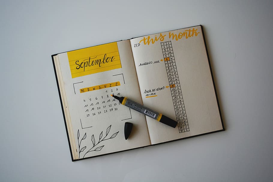 white planner with pen on top, brown book and yellow marker, bullet journal