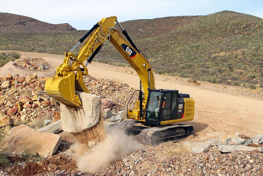 yellow and black Caterpillar excavator clipping stone on rocky hill during daytime