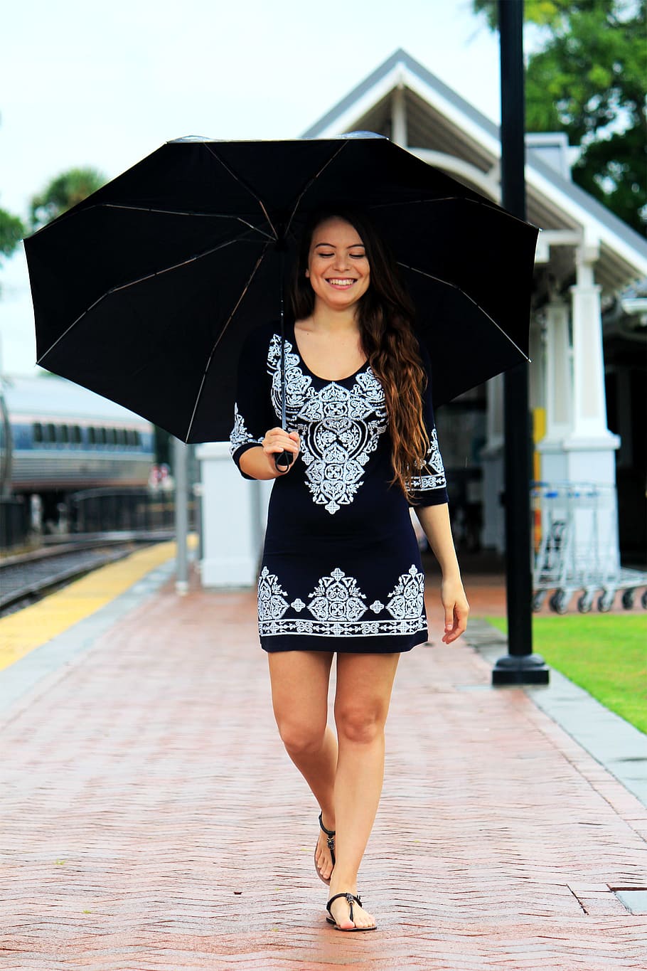 woman walking on brown pathway while holding black umbrella, woman in black and white tribal elbow-sleeved scoop-neck minidress with black umbrella walking on brown pathway during daytime