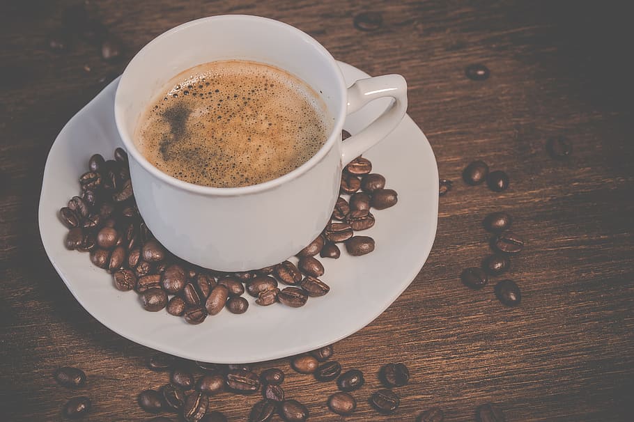 white coffee cup on saucer surrounded with coffee beans on brown wooden surface HD wallpaper