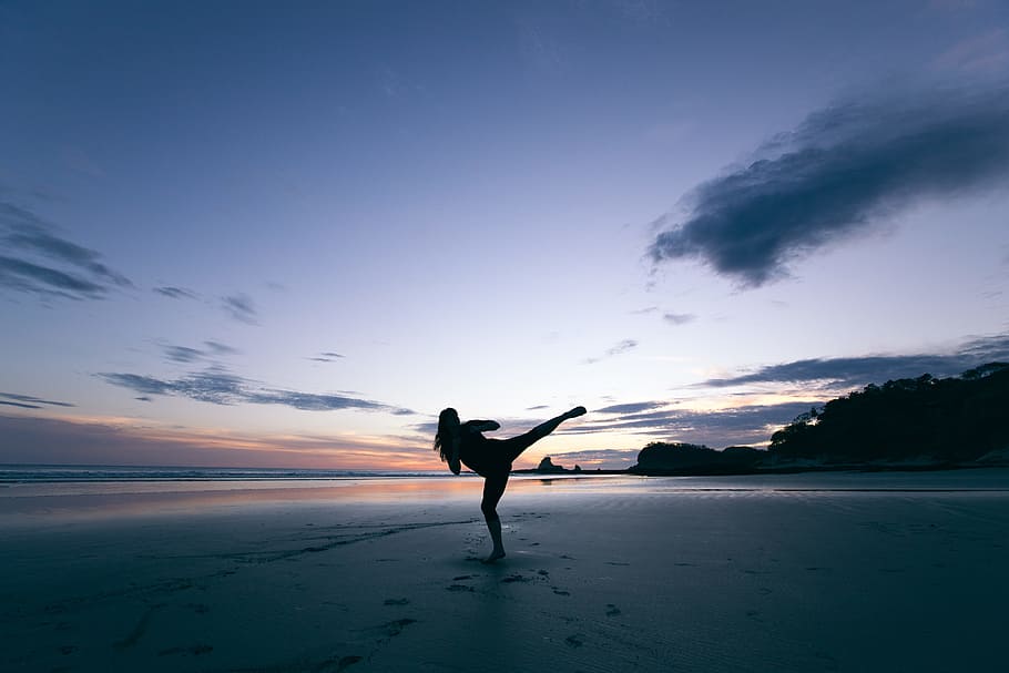 silhouette of person kicking on mid air, silhouette of person standing on seashore