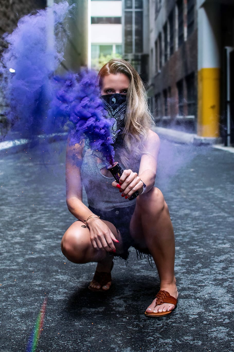 woman bending on concrete pavement holding blue smoke, woman holding purple color smoke grenade