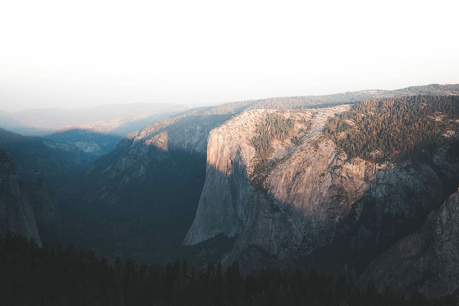 mountain cliff surrounded with trees, aerial photography of cliff under white clouds HD wallpaper