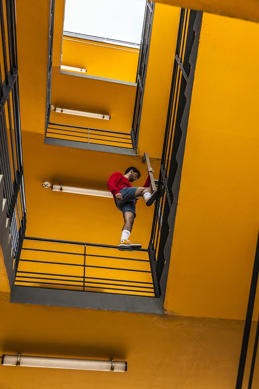 man standing on rails, man wearing red sweater standing on black metal handrail stair HD wallpaper