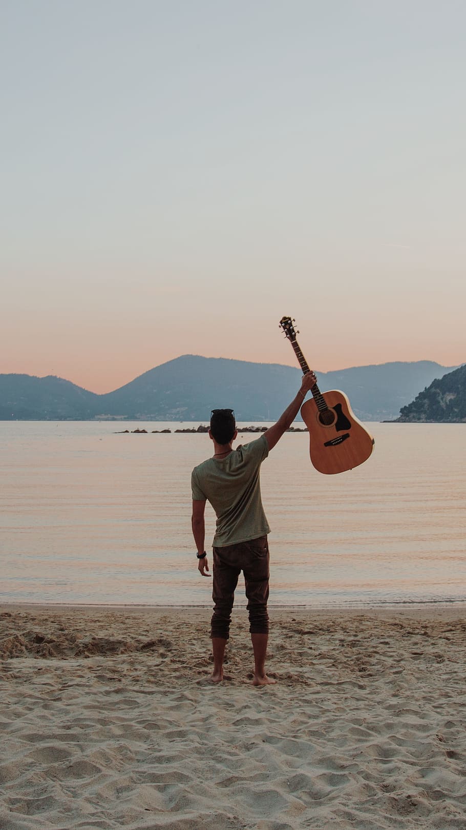man standing on seashore holding guitar raised up during daytime