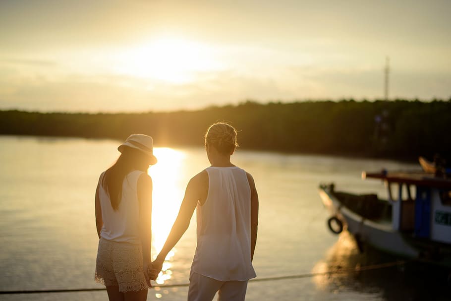 man and woman holding hand beside body of water during daytime HD wallpaper