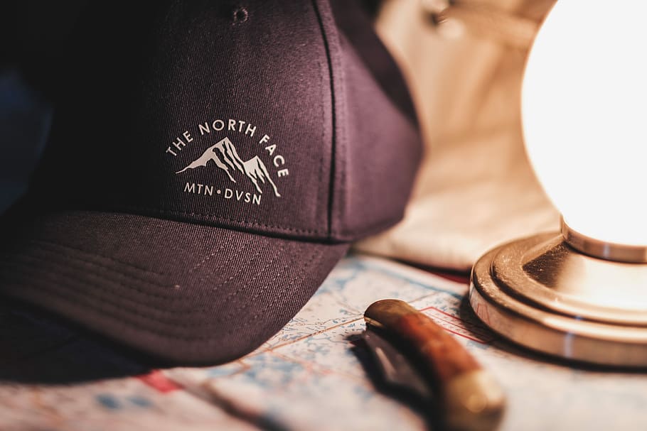 close-up photo of black and white The North Face cap beside brown pocket knife, black The North Face cap beside brown straight razor HD wallpaper