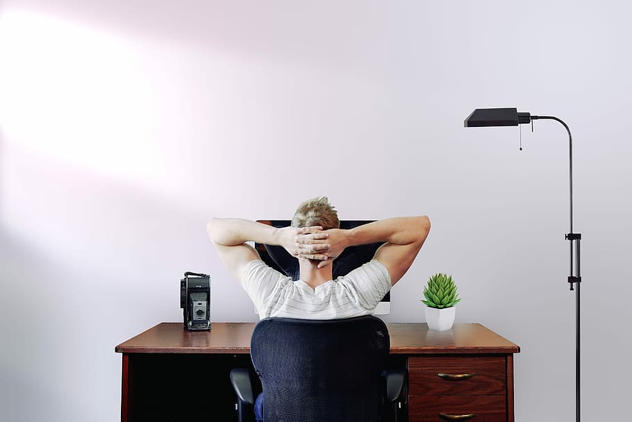 man holding his head while sitting on chair near computer desk, person sitting black swivel chair HD wallpaper