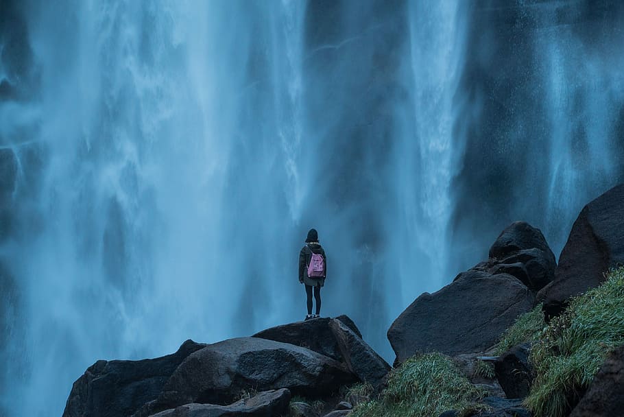 woman standing on edge waterfalls, girl with pink bag watching waterfall digital wallpaper