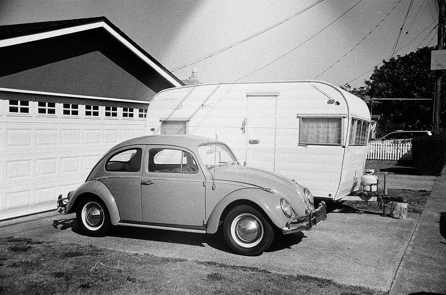 grayscale photo of Volkswagen Beetle coupe beside travel trailer parked in front of garage, grayscale photography of Volkswagen Beetle HD wallpaper