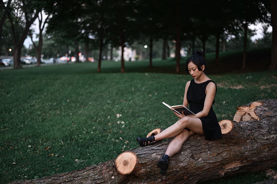 reading about meditation, woman wearing black sleeveless dress sitting on brown tree log