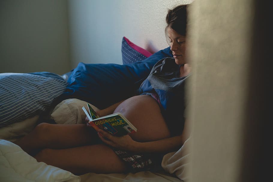 pregnant woman leaning on wall reading book while on bed, knowledge, HD wallpaper