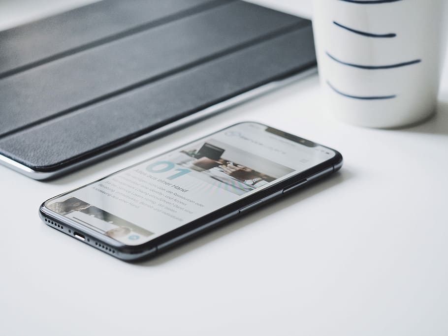 black smartphone beside black smart case, black smartphone on white board beside cup HD wallpaper