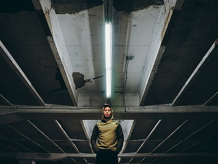low-angle photography of man wearing hooding standing on underground parking lot, man standing inside building HD wallpaper