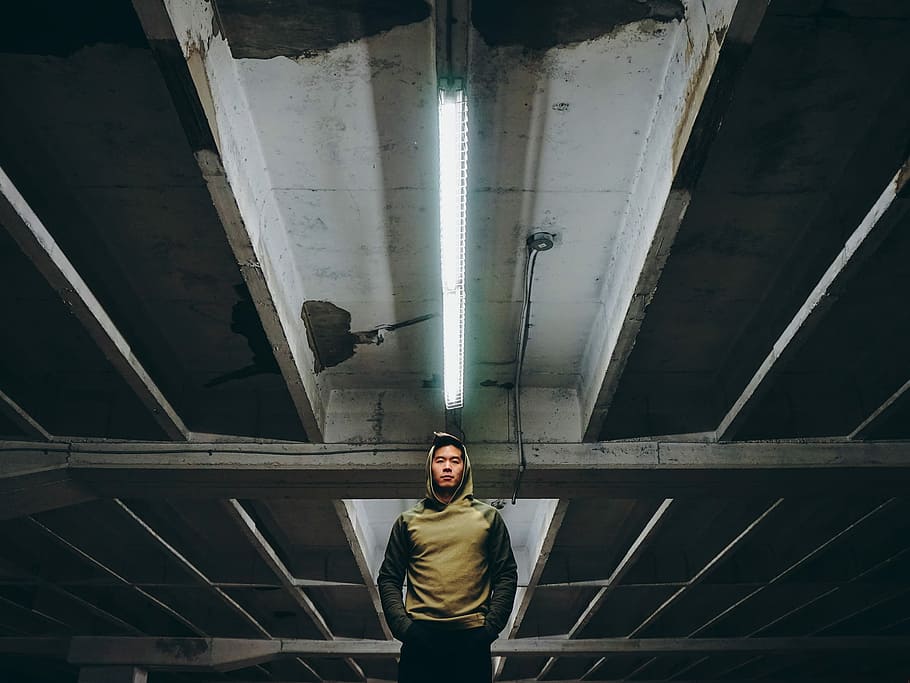 low-angle photography of man wearing hooding standing on underground parking lot, man standing inside building HD wallpaper