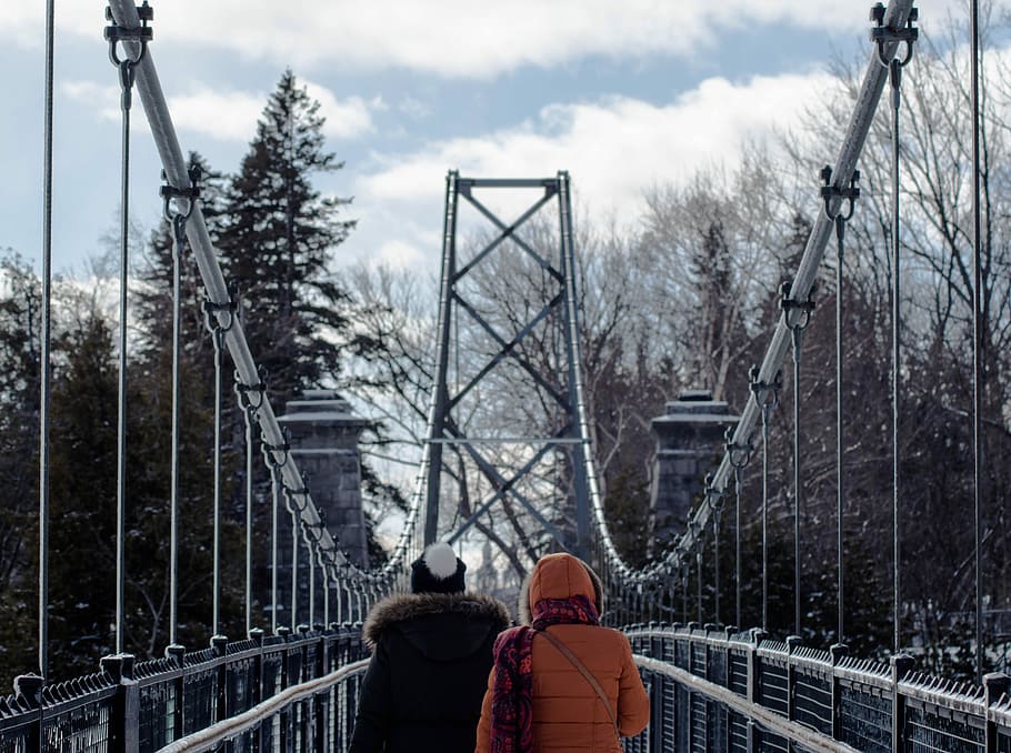 two persons walking on gray suspension bridge in between trees at daytime, two people crossing bridge HD wallpaper