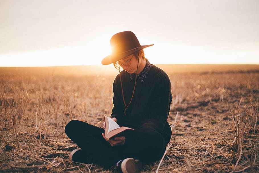 person in black sweater opening book, man sitting on ground while reading a book HD wallpaper
