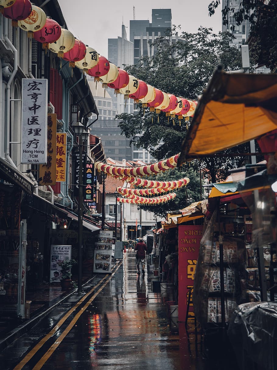assorted lanterns hanged above alleyway, man walking on wet road of China during daytime