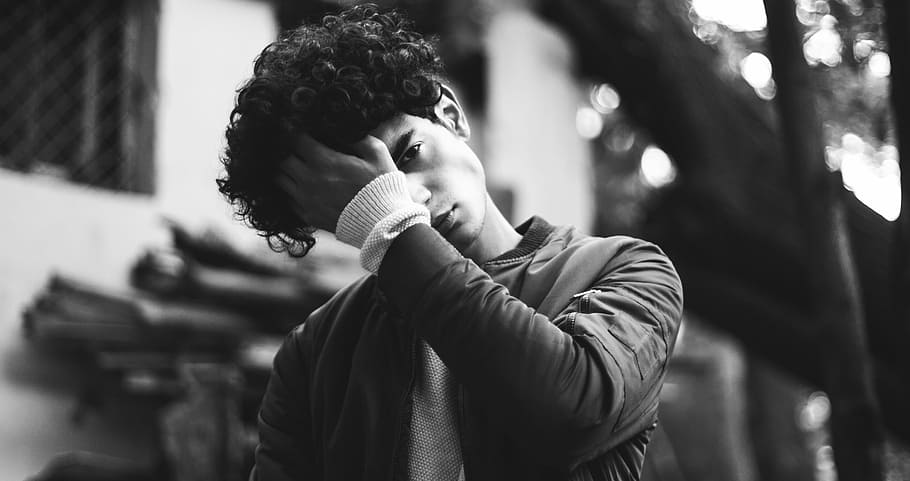 grayscale photo of man in jacket putting his palm on his forehead, man wiping up his hair