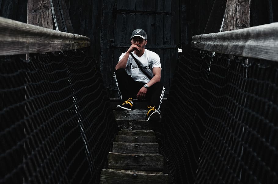 man sitting on brown surface, man in white T-shirt sitting on hanging bridge during daytime HD wallpaper