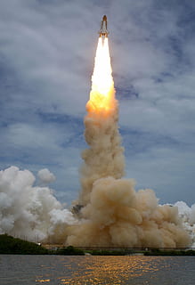 red and white space shuttle taking off near body of water under blue and white sky HD wallpaper