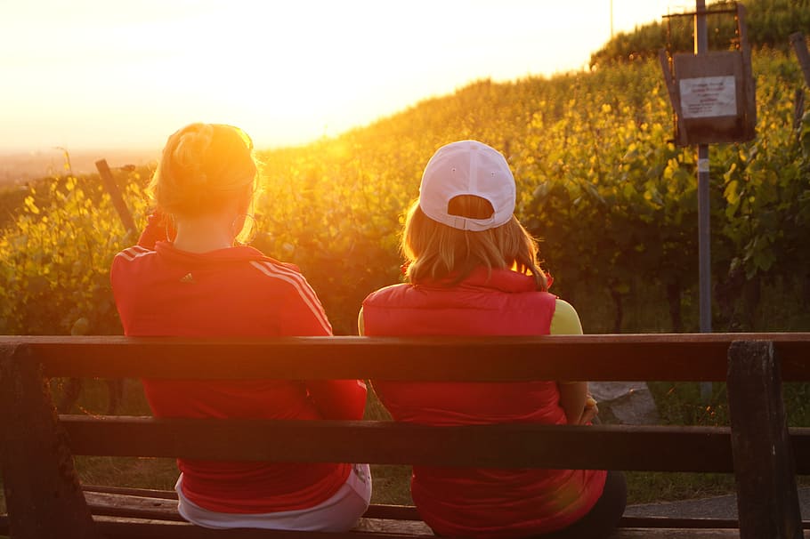two women sitting on wooden bench facing the sunlight, west HD wallpaper