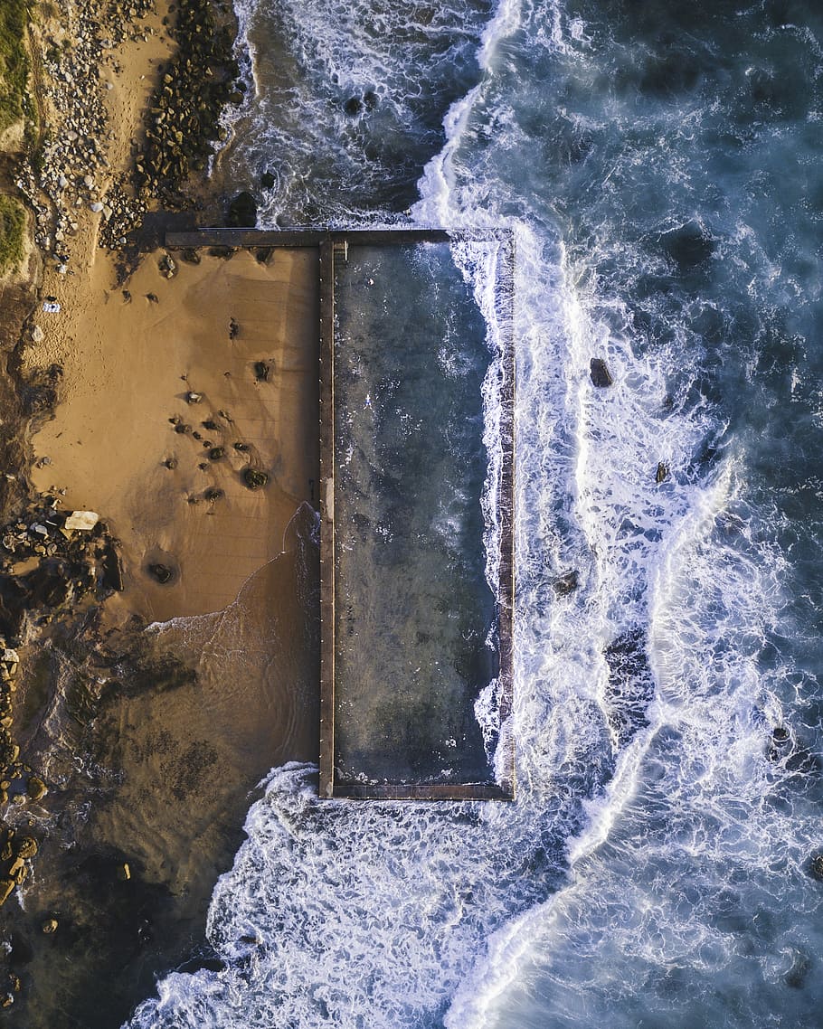 aerial photography of sea hitting sand at daytime, black rock formation near body of water during daytime