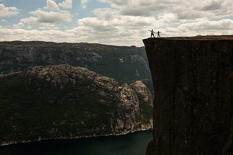 two person standing near cliff under blue and white cloudy sky during daytime HD wallpaper