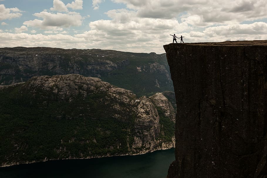 two person standing near cliff under blue and white cloudy sky during daytime HD wallpaper